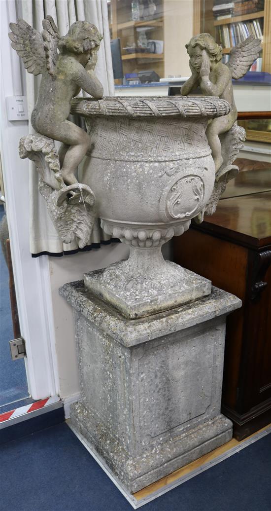 A garden urn, with cherub and goats head mounts, on square plinth, H 165cm W.90cm. (approx.)